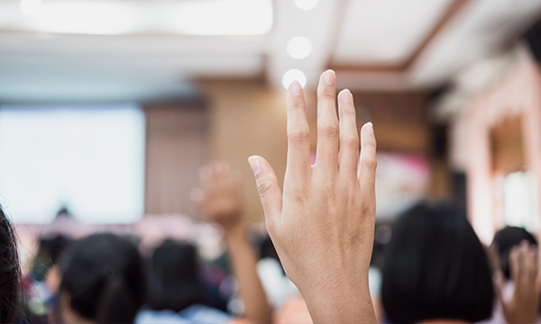 Conference auditorium audience with multiple hands raised.