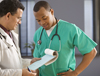 Two male healthcare providers discuss notes in clinical setting.